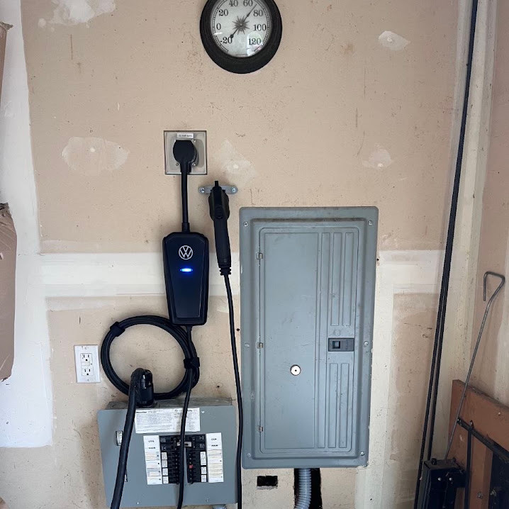 Electrical panel beside a Volkswagen EV charging unit on an unfinished wall